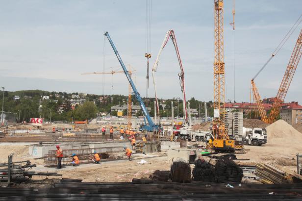 Mehrere Bauarbeiter arbeiten auf einer Baustelle mit Kränen und Betonmischern.