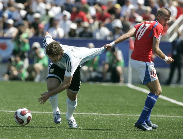 Ein Fußballspieler zieht am Trikot eines Gegenspielers, während ein Ball im Vordergrund liegt.