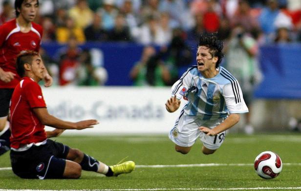 Ein argentinischer Fußballspieler springt auf dem Spielfeld, während ein chilenischer Spieler zu Boden geht.