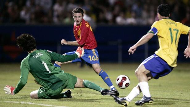 Ein Fußballspieler im roten Trikot schießt den Ball, während der Torwart versucht, ihn abzuwehren.