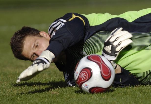 Ein Fußballtorwart hechtet auf dem Rasen nach einem Ball.