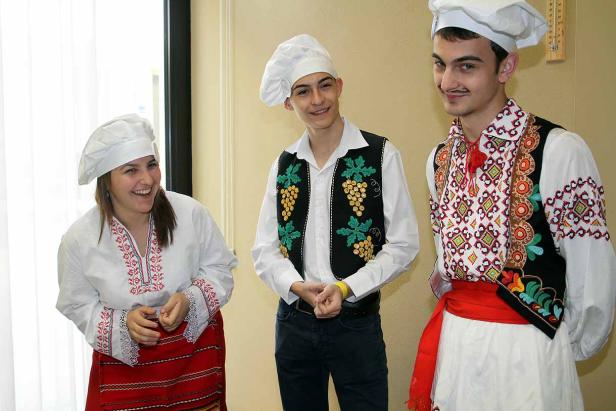 Drei Personen in Kochmützen und traditioneller bulgarischer Kleidung stehen zusammen.