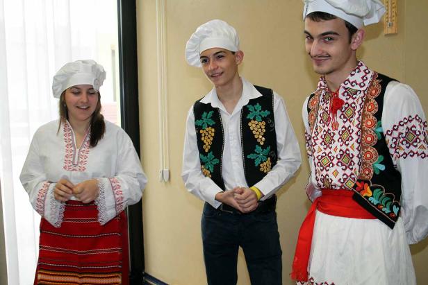 Drei Personen in Kochmützen und traditioneller bulgarischer Tracht stehen nebeneinander.