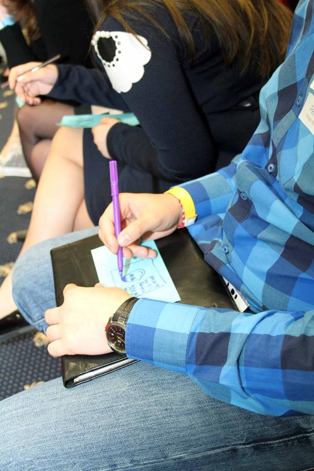 Eine Person in einem blauen Hemd macht Notizen mit einem lila Stift.