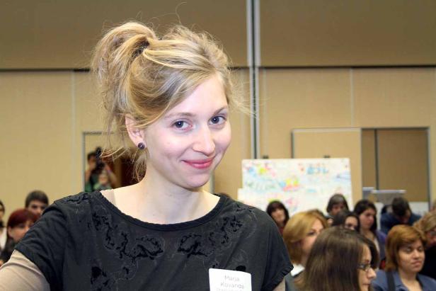 Eine lächelnde Frau, möglicherweise namens Maria Kovanda, steht vor einer Gruppe von Menschen.