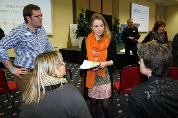 Eine Frau mit orangefarbenem Schal spricht vor Publikum.