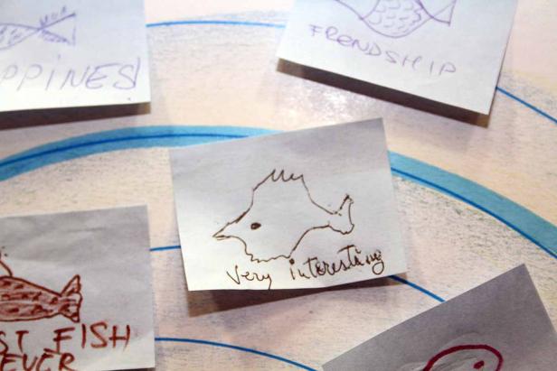 Mehrere Notizen mit Fischzeichnungen und handschriftlichen Texten liegen auf einer Oberfläche.