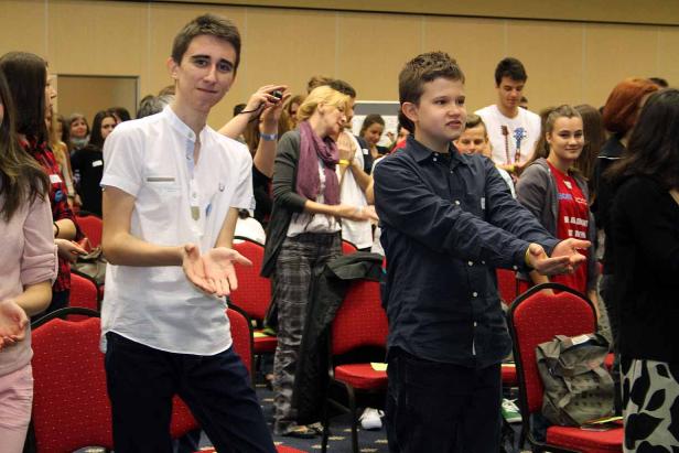 Eine Gruppe junger Leute steht in einem Raum und macht Handbewegungen.