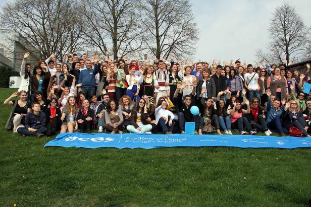 Eine große Gruppe von Menschen posiert für ein Foto im Freien und winkt.