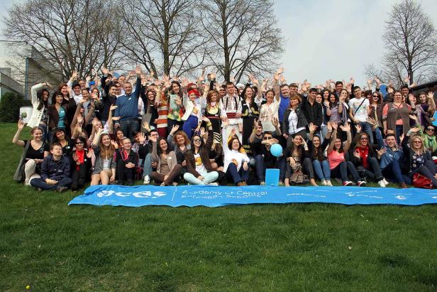Eine große Gruppe von Menschen winkt vor einem Banner der „Academy of Central European Schools“.