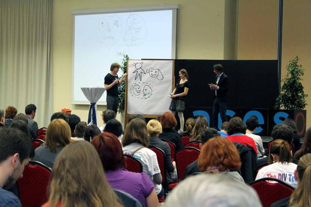 Zwei Personen präsentieren Zeichnungen vor einem Publikum.