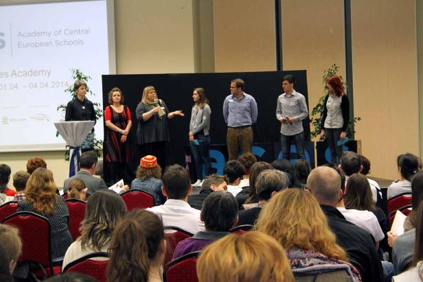 Eine Gruppe von Personen steht auf einer Bühne vor einem Publikum.