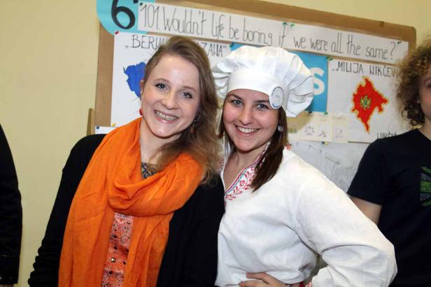 Zwei lächelnde junge Frauen stehen vor einer Tafel mit dem Slogan „Wouldn't life be boring if we were all the same?“.
