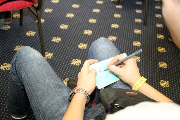 Eine Person zeichnet ein Gesicht auf ein blaues Blatt Papier.