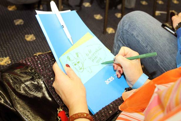 Eine Frau zeichnet und schreibt auf einem Notizblock mit dem Aufdruck „aces“.