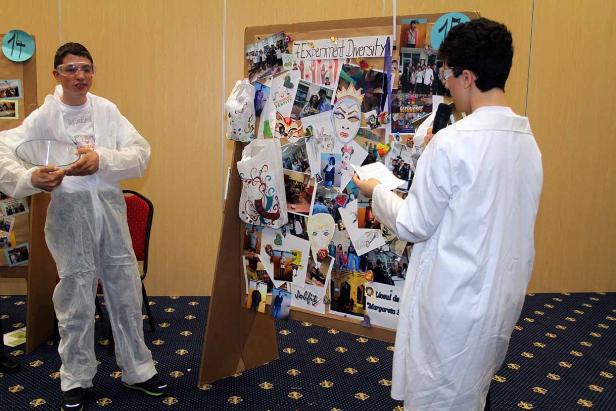 Zwei Jugendliche in Laborkitteln präsentieren ein Projekt zum Thema „Experiment Diversity“.