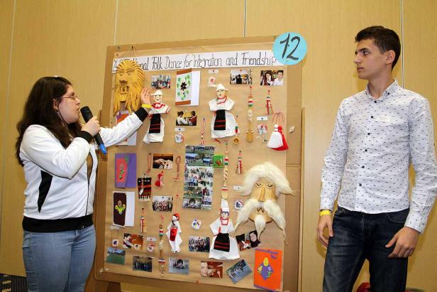 Eine Frau präsentiert mit einem Mikrofon eine Ausstellung über Volkstänze und Freundschaft.