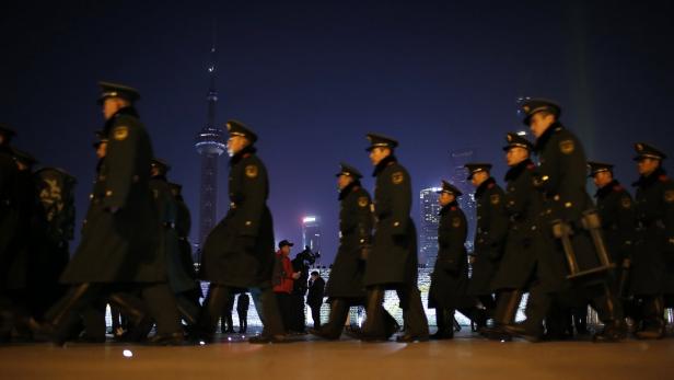 Eine Gruppe von Polizisten marschiert nachts vor der Skyline von Shanghai.