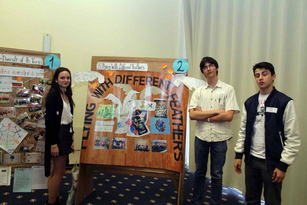 Drei Jugendliche stehen vor zwei Präsentationswänden mit dem Titel „Flying With Different Feathers“.