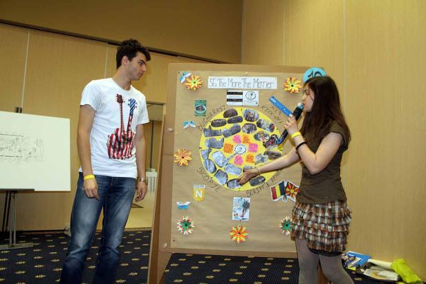 Eine junge Frau präsentiert ein Projekt vor einem Publikum, mit Hinweisen auf Bukarest und Skopje.