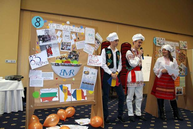 Drei Personen in Trachten stehen vor einer Präsentationstafel mit dem Titel „The BMR's Salad Bowl“.