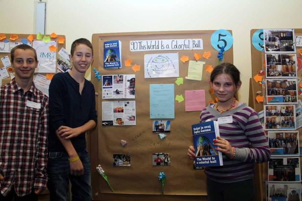 Drei Jugendliche stehen vor einer Pinnwand zum Thema „The World is a Colorful Ball“.
