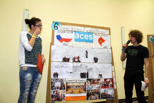 Zwei Jugendliche präsentieren ein Projekt mit Zeichnungen und Fotos auf einem Aufsteller.