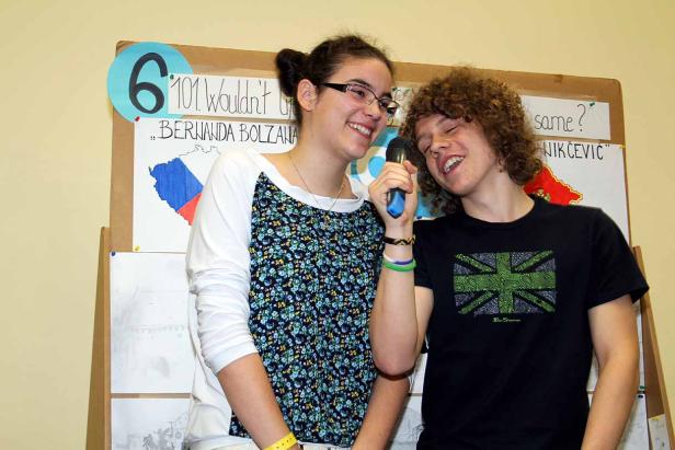 Zwei Jugendliche singen zusammen in ein Mikrofon vor einer Tafel.