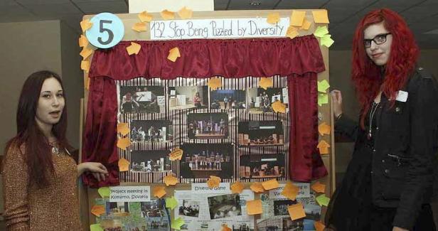 Zwei junge Frauen präsentieren eine Tafel zum Thema Diversität mit Fotos und Notizen.