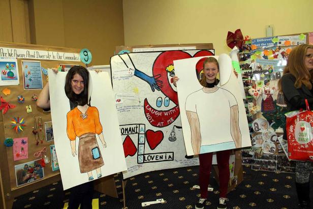 Zwei Mädchen halten bemalte Pappfiguren vor ihre Körper.