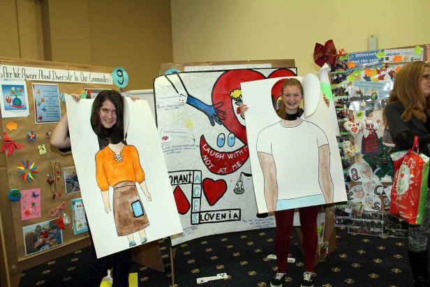 Zwei Mädchen halten bemalte Pappfiguren vor ihre Körper.