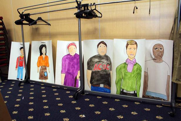 Eine Kleiderstange mit daran aufgehängten, bemalten Porträts von verschiedenen Personen.