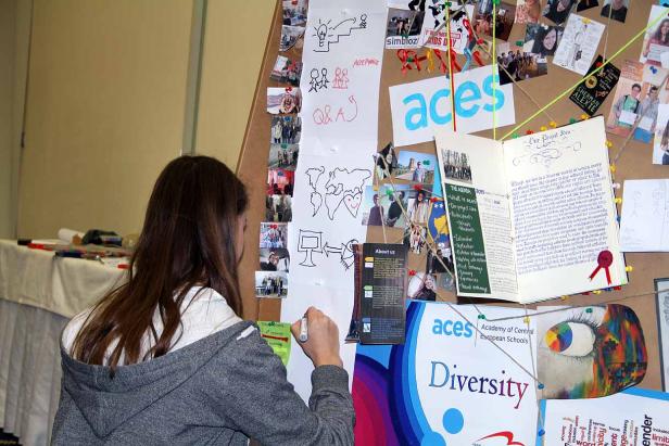 Eine junge Frau schreibt auf ein Blatt Papier vor einer Pinnwand mit Fotos und Notizen zum Thema Vielfalt.
