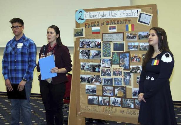 Drei Personen stehen vor einer Tafel mit dem Titel „Faces of Diversity“.