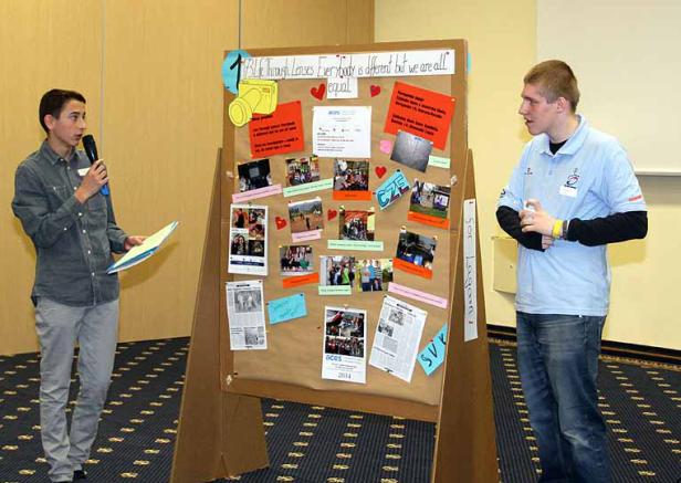 Zwei junge Männer präsentieren eine Collage mit dem Titel „Life Through Lenses: Everybody is different but we are all equal“.