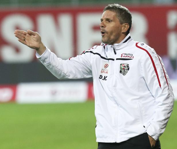 Ein Fußballtrainer gestikuliert während eines Spiels am Spielfeldrand.