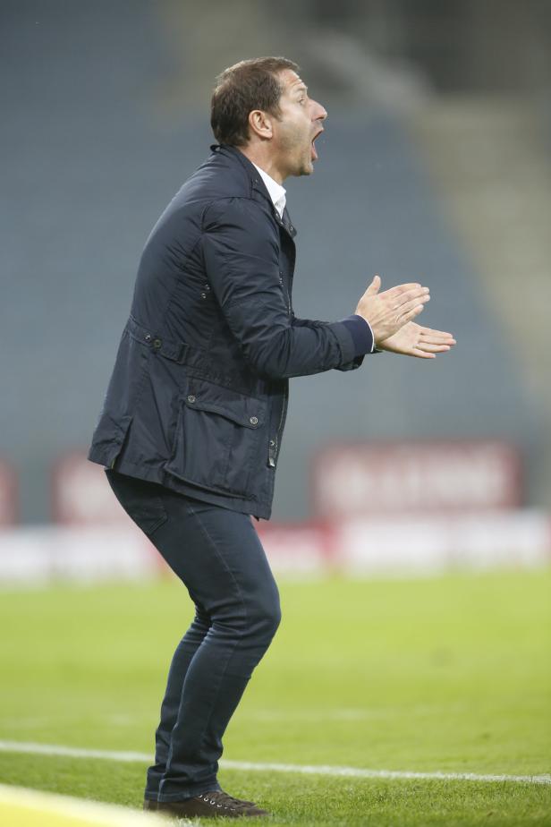 Ein Fußballtrainer gestikuliert und schreit am Spielfeldrand.