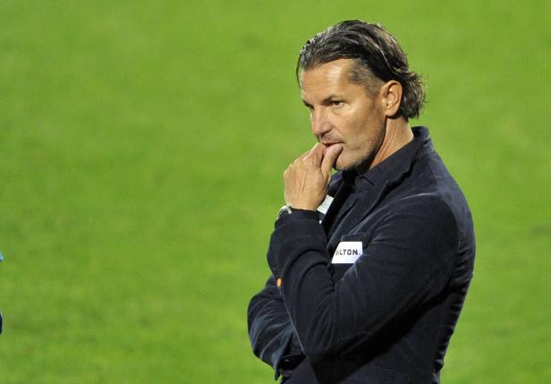 Ein nachdenklicher Mann in einer dunklen Jacke steht vor einem grünen Hintergrund.