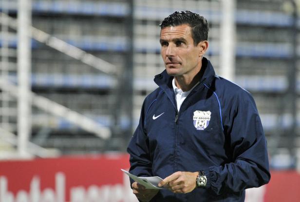 Ein Mann in einer Jacke des SV Grödig hält ein Blatt Papier in der Hand.