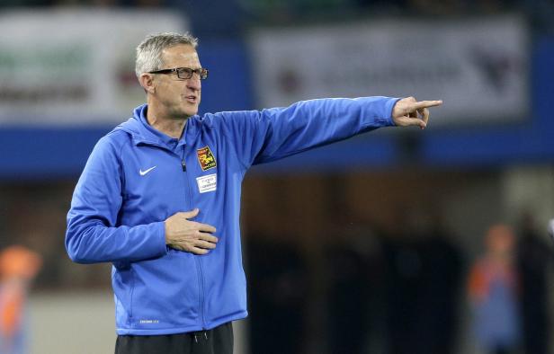 Trainer mit Brille und blauer Jacke gestikuliert auf dem Spielfeld.