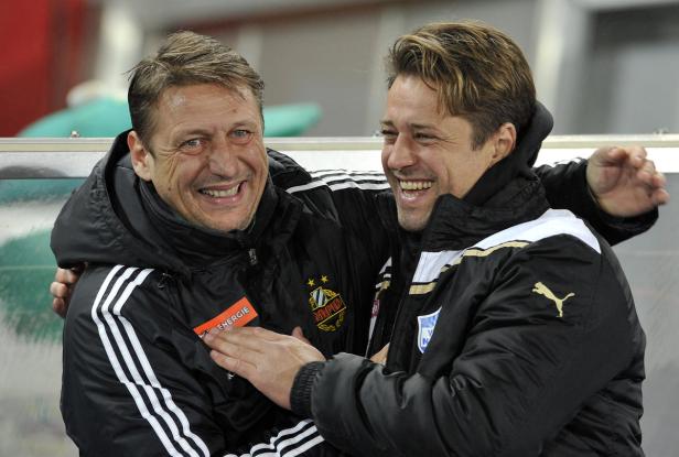 Zwei lachende Männer in Sportjacken umarmen sich.