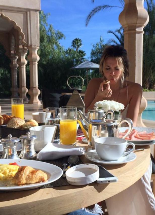 Eine Frau genießt ein Frühstück im Freien mit Croissant, Saft und Kaffee.