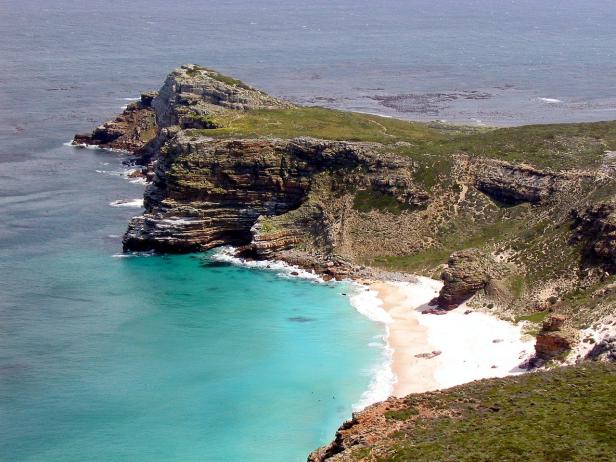 Blick auf eine Küstenlandschaft mit Klippen, einem Strand und türkisfarbenem Wasser.