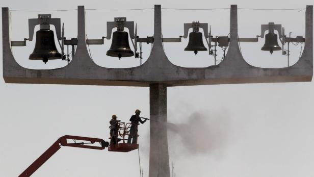 Zwei Arbeiter reinigen mit einem Hochdruckreiniger ein Glockenspiel auf einem hohen Denkmal.