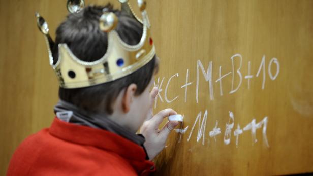 Ein Junge mit Krone schreibt mit einem Stift auf eine Tafel.