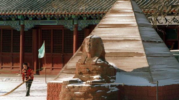 Eine Sphinx-Statue und eine Pyramide stehen vor einem traditionellen chinesischen Gebäude, während eine Person kehrt.