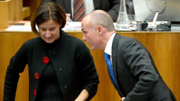 Ein Mann im Anzug beugt sich zu einer Frau mit roter Brosche.