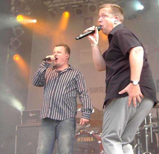 Zwei Männer singen auf einer Bühne in Mikrofone.