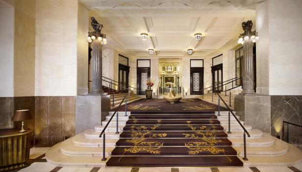 Die prunkvolle Lobby eines Hotels mit einer breiten Treppe und Marmorsäulen.