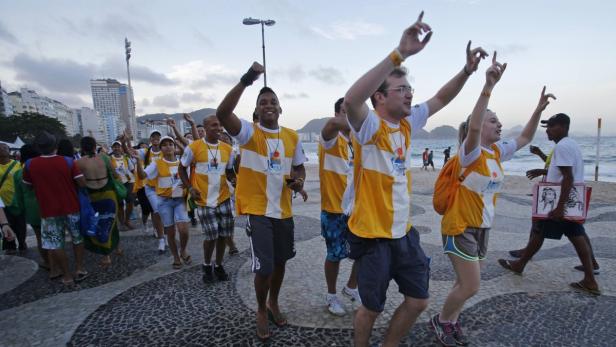 Eine Gruppe von Menschen in gelben T-Shirts tanzt und feiert am Strand von Rio de Janeiro.